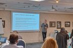 Fotografie din timpul cursului. Participanții sunt asezați la mese, unii dintre ei poarta căști pentru traducere. Profesorul Bach prezintă pe ecran unul dintre slide-urile cursului: „Luarea, sprijinul și realizarea deciziilor.” Michael Bach este un bărbat între două vârste, înalt, cu părul cărunt, tuns scurt.